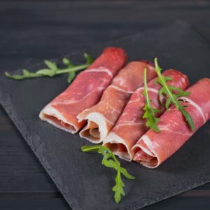 Black stone platter with slices of cured ham or Spanish jamon serrano or Italian prosciutto crudo